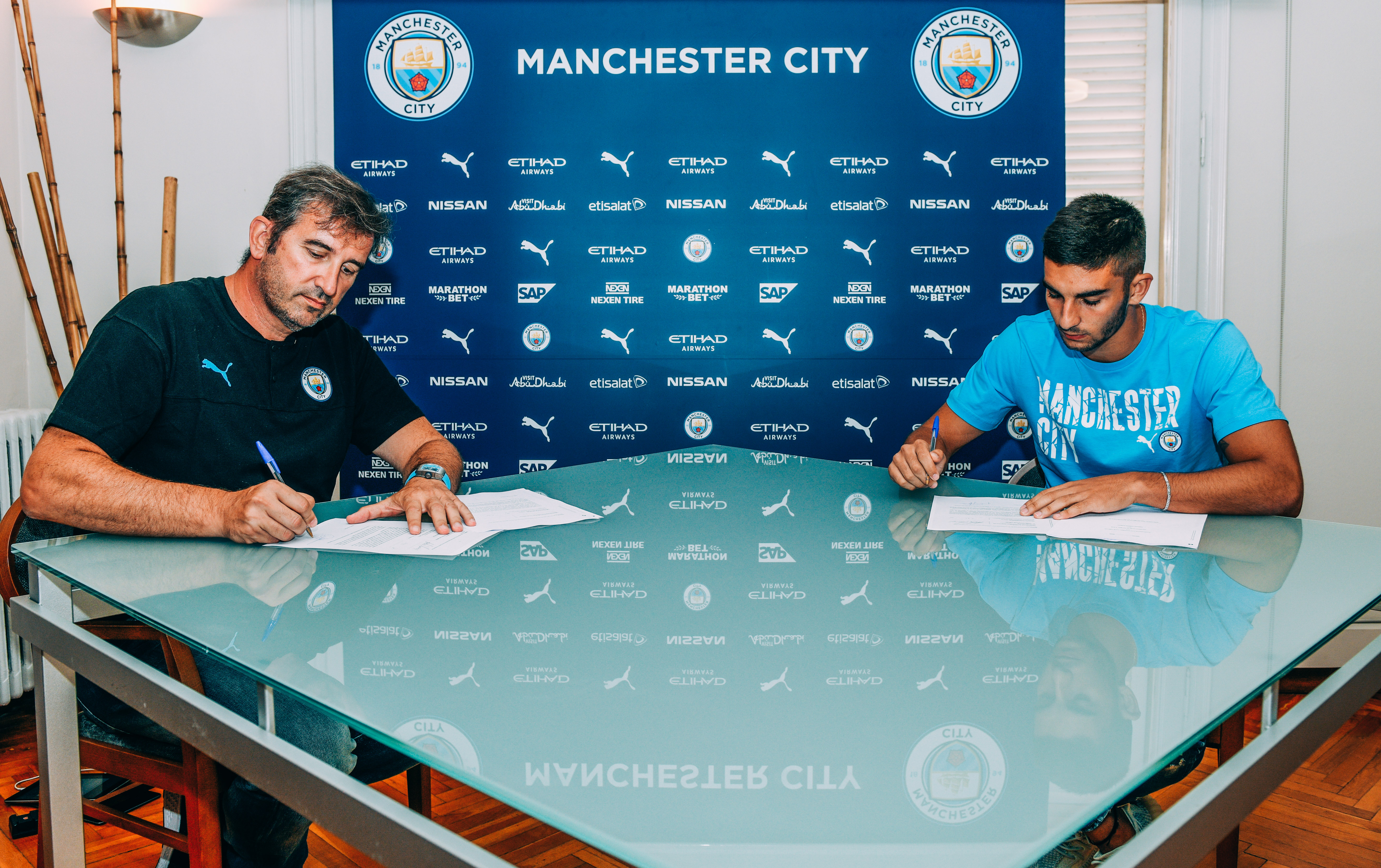 
                        FIRMA. : Ferran Torres firma su contrato con el Manchester City junto a Ferran Soriano.
                